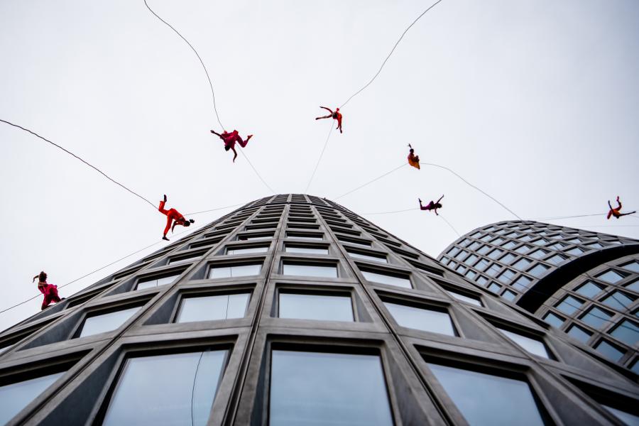 On the side of a round building, six folks are strung up and appear to bounce off of the building.
