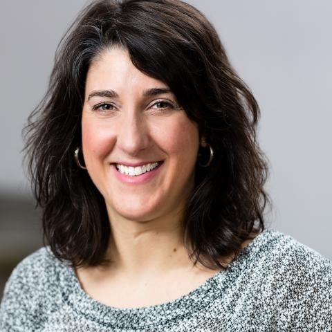 a white woman with shoulder length dark hair wearing a grey top.